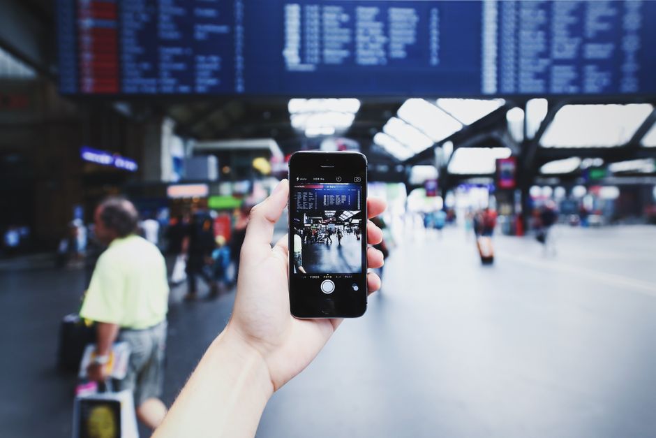 The owner of a modern, clean-looking US coffee shop smiles while looking at a photo of a tropical beach on their smartphone, representing the travel goal that motivates their work.