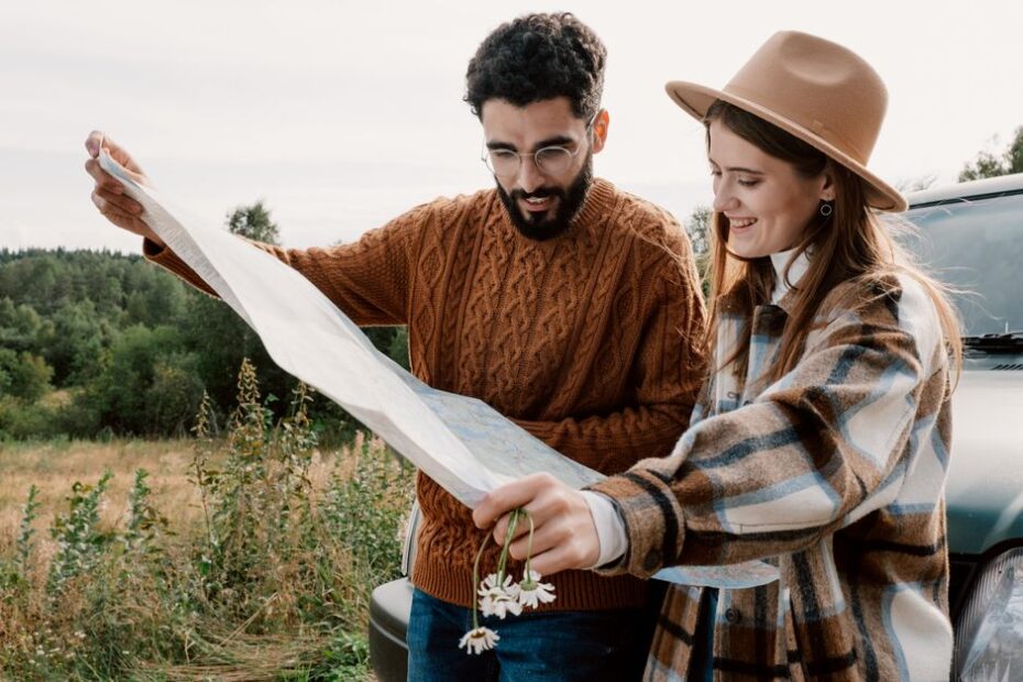 Professional couple sits at a bright, modern desk, looking at a laptop with business plans while a world map and passports...