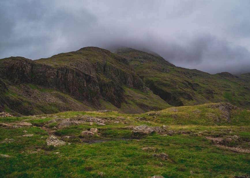 Traveler stands alone in a misty Lake District valley, looking down at a map, symbolizing the challenge of finding one's w...