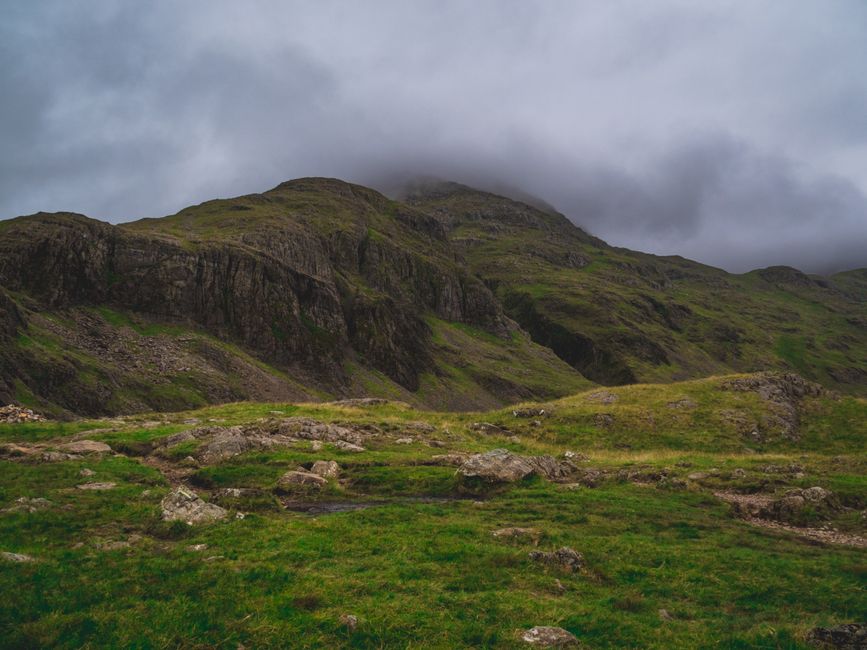 Traveler stands alone in a misty Lake District valley, looking down at a map, symbolizing the challenge of finding one's w...