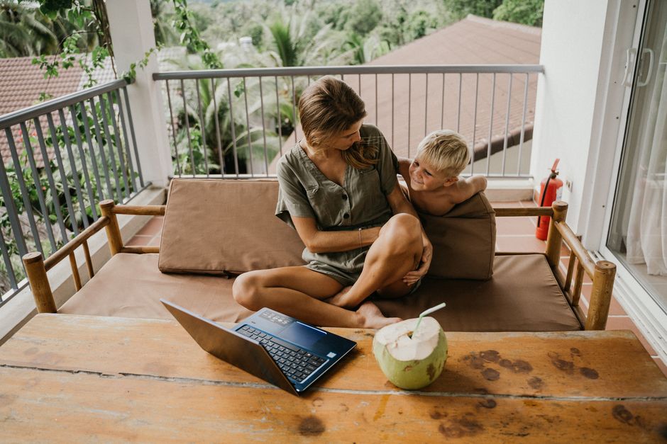 A woman casually works on her laptop on a sunlit hotel balcony overlooking a beautiful ocean, embodying the freedom and lifestyle funded by a successful franchise investment.
